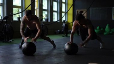 Spor salonunda, iki kendini adamış sporcu antrenmanlarını geliştirmek için ilaç toplarını kullanarak zorlu şınav çekerler.