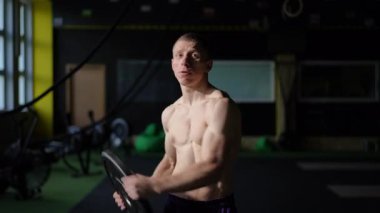 İyi yapılı ve kaslı bir atlet spor salonu ortamında çeşitli yoğun ağırlık disk egzersizleri sergiliyor.