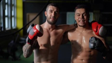 Kendini işine adamış iki boksör, güven içinde antrenman giysileriyle poz veriyor, yoldaşlıklarını ve atletizmlerini sergiliyorlar.