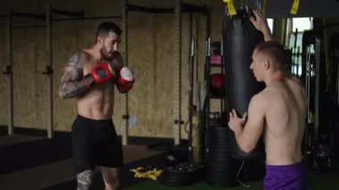 Canlı bir spor salonunda, iki sporcu ağır bir torba kullanarak boks tekniklerini yoğun bir şekilde eğitiyorlar.