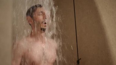 Bir adam serinletici ve canlandırıcı bir duşun keyfini çıkarırken su üzerine sıçrıyor ve deneyimini geliştiriyor.