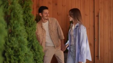 Çağdaş ahşap bir alandaki yeşillikle etkileşime giren bir çift, bağlantı ve merak gösteriyor..