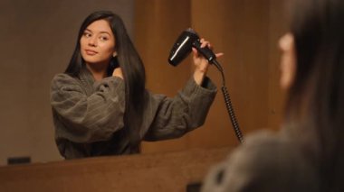 Bir kadın zarif bir şekilde saçını saç kurutma makinesiyle şekillendirir, zarafetini, özgüvenini ve güzelliğini gösterir.