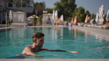 Bir grup arkadaş güneşli bir günde lüks bir havuzun etrafında uzanarak harika vakit geçiriyorlar.