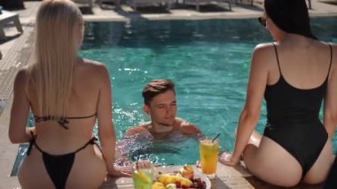 Canlı ve canlı bir havuz kenarı sahnesi gençlik rahatlığı, ferahlatıcı içecekler ve sıcak güneş ışığı sergiliyor.