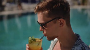 Şık bir genç adam sıcak güneşin altında havuzun kenarında serinletici bir tropikal içeceğin tadını çıkarıyor.