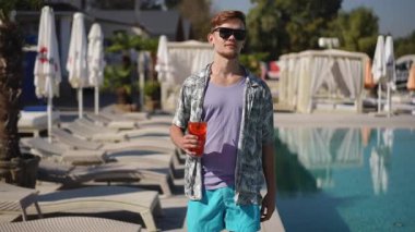 Genç bir adam, canlı bir havuz başında son moda akımlarını sergileyerek serinletici içeceklerin tadını çıkarıyor.