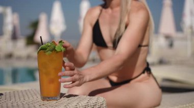 Havuz kenarında bikinili ferahlatıcı bir yaz içkisinin olduğu sakin bir sahne hayal edin.
