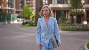 Parlak mavi takım elbiseli şık bir kadın özgüvenle modern bir şehir ortamında yürüyor.