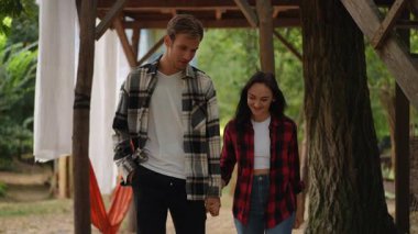 Genç bir çift el ele tutuşuyor, ışıl ışıl gülümsüyor ve dışarıda sakin bir ortamda vakit geçirmenin tadını çıkarıyorlar.