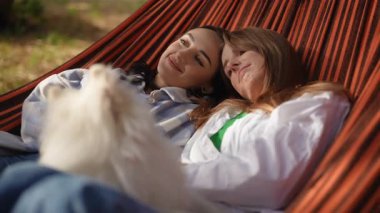 Güneşli bir günde, iki yakın arkadaş hamakta neşeli bir şekilde vakit geçiriyorlar.