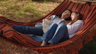 İki yakın arkadaş güneşin altındaki hamakta rahat bir anın tadını çıkarıyorlar. Etrafı tüylü köpekleriyle çevrili.