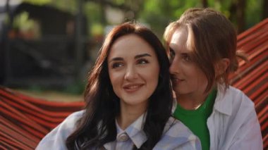 İki gülen arkadaş, güzel doğayla çevrili sıcacık bir hamakta keyifle vakit geçiriyorlar.