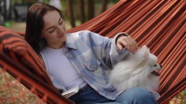Bir kadın, dışarıda bir hamakta dinlenirken sevimli pomeranya köpeğiyle güzel vakit geçirmekten zevk alır.