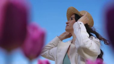 Bir kadın saman şapkasını renkli çiçek açan lalelerin arasına yerleştirir. Canlı, güzel bir açık hava ortamında.