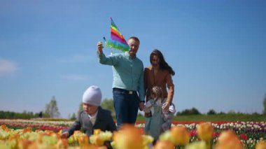 Gökkuşağı uçurtması uçururken renkli ve canlı bir lale tarlasında geçirilen keyifli ve eğlenceli bir aile günü.