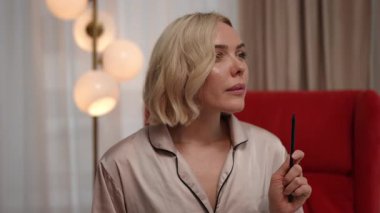 Lüks ipek pijamalı bir kadın sakince elinde kalemle oturur ve çeşitli fikirleri düşünür.