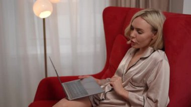 Lüks ipek pijama giymiş şık ve şık bir kadın dizüstü bilgisayarıyla çağdaş bir ortamda meşgul.