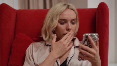 Bir kadın şık bir sandalyede otururken akıllı telefonuyla uğraşırken farklı duygular ifade eder.