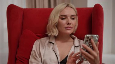 Bir kadın şık ve şık kırmızı bir sandalyede otururken rahat ve tesadüfen akıllı telefonuyla meşgul olur.