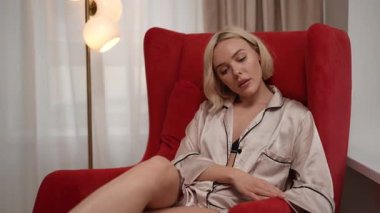 Huzurlu bir ortamda, neşeli bir kadın arkasına yaslanır, şık kırmızı koltuğunda nefis bir içkinin tadını çıkarır.