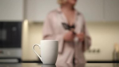 Huzurlu ve uyumlu bir sabah sahnesi beyaz bir kahve fincanını düşünceli bir şekilde mutfak tezgahına koyuyor.