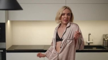 Bir aktris zarif, modern bir mutfakta poz verirken şık bir elbise giyer, zarafet ve güzellik yayar.