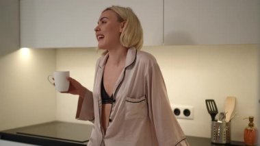 Bir kadın sabah kahvesini zevkle yudumlar şık ve güzel tasarlanmış bir mutfakta, günlük zarafetini sergiler.