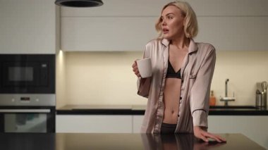 Şık ve modern bir mutfakta şık bir kadın sabah kahvesinin tadını çıkarıyor. Saf pozitiflik ve neşe saçıyor.