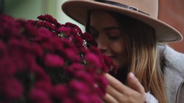 Genç bir kadın neşeyle gülümsüyor, hoş bir ortamda canlı mor çiçeklerin hoş kokusunun tadını çıkarıyor.