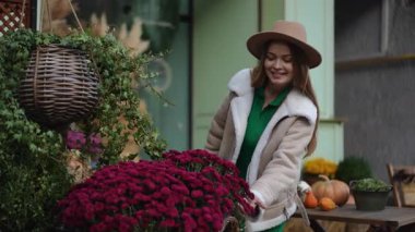 Zarif bir kıyafet giymiş neşeli bir kadın, resimli bir sonbahar ayininin ortasında canlı bir çiçek sergisinden hoşlanıyor.