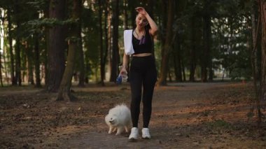 Ağır çekim. Aktif bir kadın, huzurlu bir orman ortamında tüylü köpeğiyle keyifli bir yürüyüş yapmaktan zevk alır.