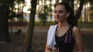 Ağır çekim. Genç bir kadın, kulaklıklarla donatılmış ve su şişesi olan açık hava egzersizlerinden hoşlanır.