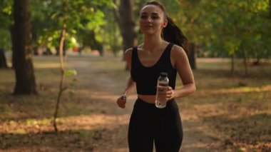 Ağır çekim. Genç bir kadın neşeyle çarpıcı bir parkta koşuyor, doğadayken spor rutinini tamamen benimsiyor.