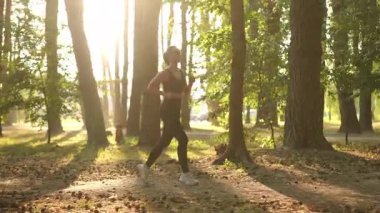Bir kadın, sıcak, altın güneş ışığıyla aydınlatılmış, nefes kesici, güzel ormanda koşmaktan mutlu olur.