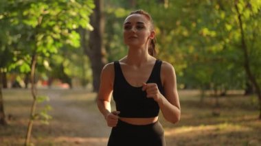 Canlı yeşil bir parkta koşan bir kadın, doğaya dalmışken sağlığını ve canlılığını gösteriyor.