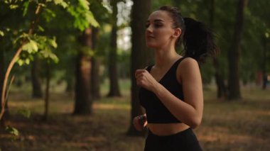 Ağır çekim. Formda bir kadın enerjik bir şekilde güneşli bir ormanda koşar. Macera ve sağlığı somutlaştırır, neşe verir.