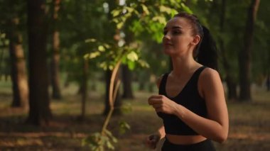 Bir kadın enerjik bir şekilde yemyeşil bir ormanda koşar. Hem zindelik hem de sükuneti somutlaştırır.