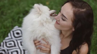 Güzel çimenli bir bölgede, bir kız sevimli pomeranyasını neşeyle kucaklıyor, saf sevgi ve mutluluk sergiliyor.