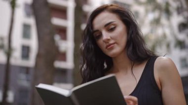Genç bir kadın sakin bir şehir ortamında büyüleyici bir kitaptan zevk alıyor, doğa ve edebiyat karışımı.
