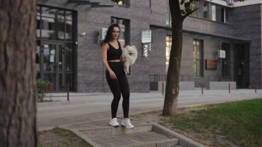 Şık bir kadın, tüylü köpeğiyle modern mimarinin ortasında rahatça dolaşmaktan zevk alır.