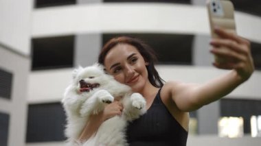Neşeli bir kadın tüylü köpeğiyle parlak bir selfie çeker, doğada harika bir anı yakalar.