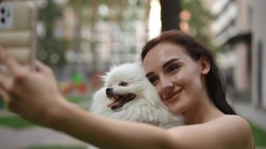 Bir kadın, sevimli Pomeranya köpeğiyle canlı bir açık hava ortamında eğlenceli ve eğlenceli bir selfie çeker.