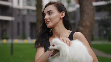 Bir kadın sevimli küçük beyaz Pomeranya 'lısını neşeyle kucağına alır, saf mutluluğu yakalar güzel yeşil, yemyeşil bir parkta.