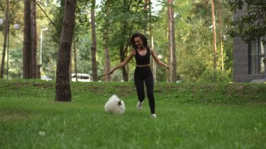 Bir kadın güzel ve huzurlu bir park ortamında tüylü köpeğiyle enerjik ve sağlıklı bir yürüyüşün tadını çıkarıyor.