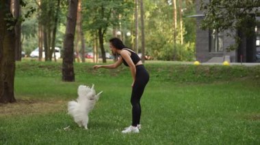Bir kadın, hayat dolu güzel, canlı yeşil bir parkta tüylü köpeğiyle neşeli anlar yaşamaktan zevk alır.