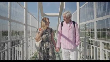 Madrid 'li yaşlı bir adam eşiyle el ele tutuşarak modern yaya köprüsünden geçiyor. Birbirlerine gülümserler, bağlantının ve güneşin tadını çıkarırlar..