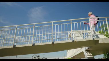 Madrid 'den gelen gülümseyen son sınıf öğrencisi, beyaz bir yaya köprüsünde, mavi gökyüzünün altında, geçmekte olan bir kadınla şakacı bir şekilde dans ediyor, anlık bir neşe anı paylaşıyor..