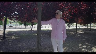 Madrid 'li son sınıf öğrencisi pembe gömlekli ve güneş gözlüklü bir ağaç gövdesine hafifçe bastırıyor, dayanıklılığını test ederken yapraklı gölgeli bir parkta sakin bir yürüyüş yapıyor..