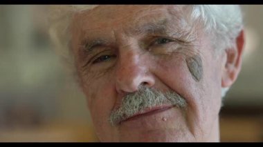 Yüzünde alaycı bir ifade olan yaşlı bir adamın kamera önünde sanki biriyle flört ediyormuş gibi göz kırpması ve öpüşmesi.